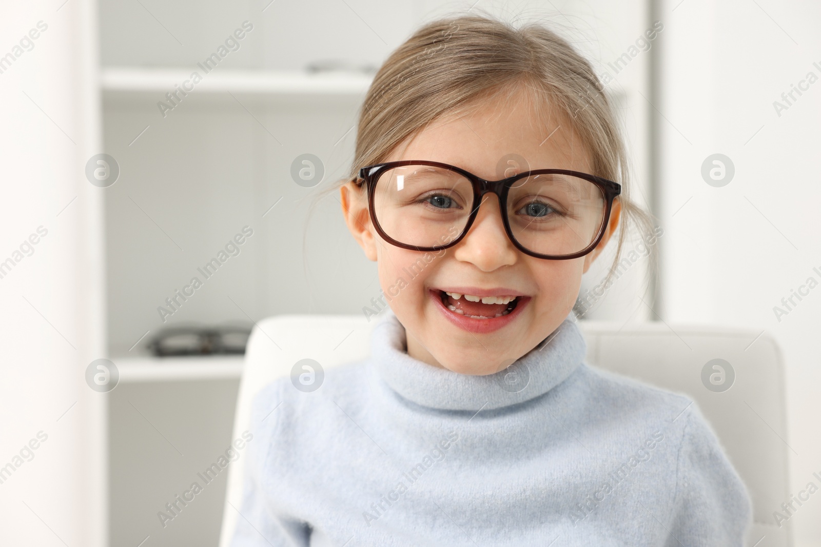 Photo of Little girl trying glasses at ophthalmologist office, space for text