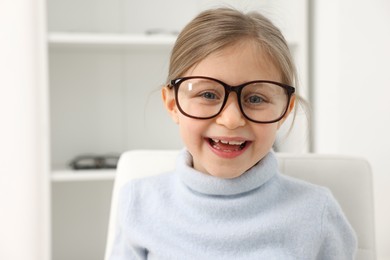 Little girl trying glasses at ophthalmologist office, space for text