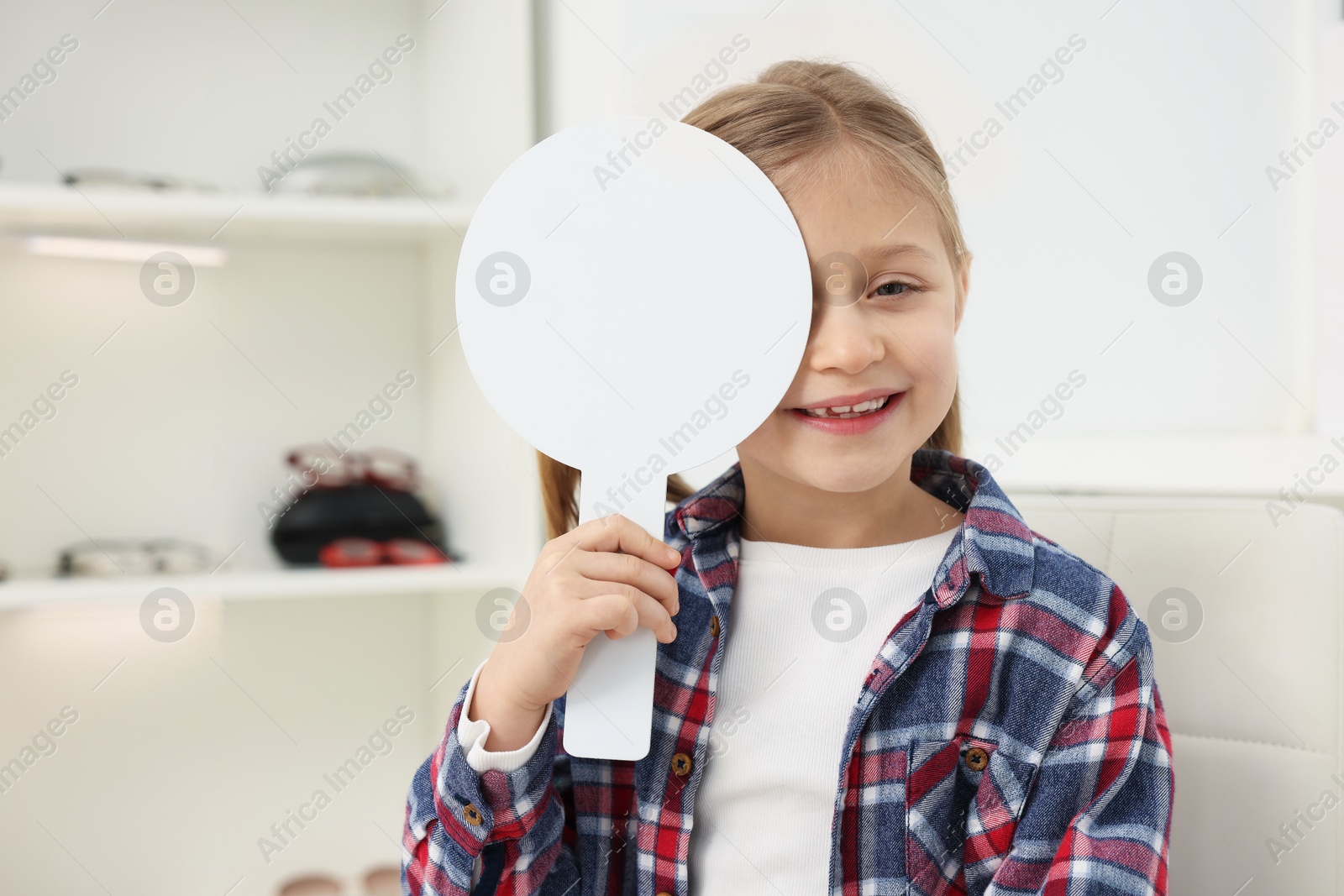 Photo of Little girl covering her eye at ophthalmologist office, space for text