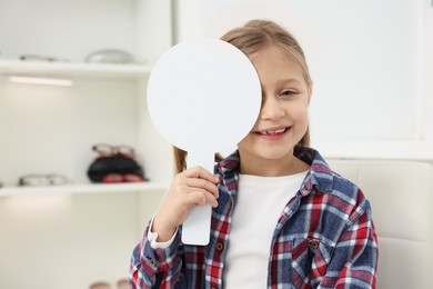 Photo of Little girl covering her eye at ophthalmologist office, space for text