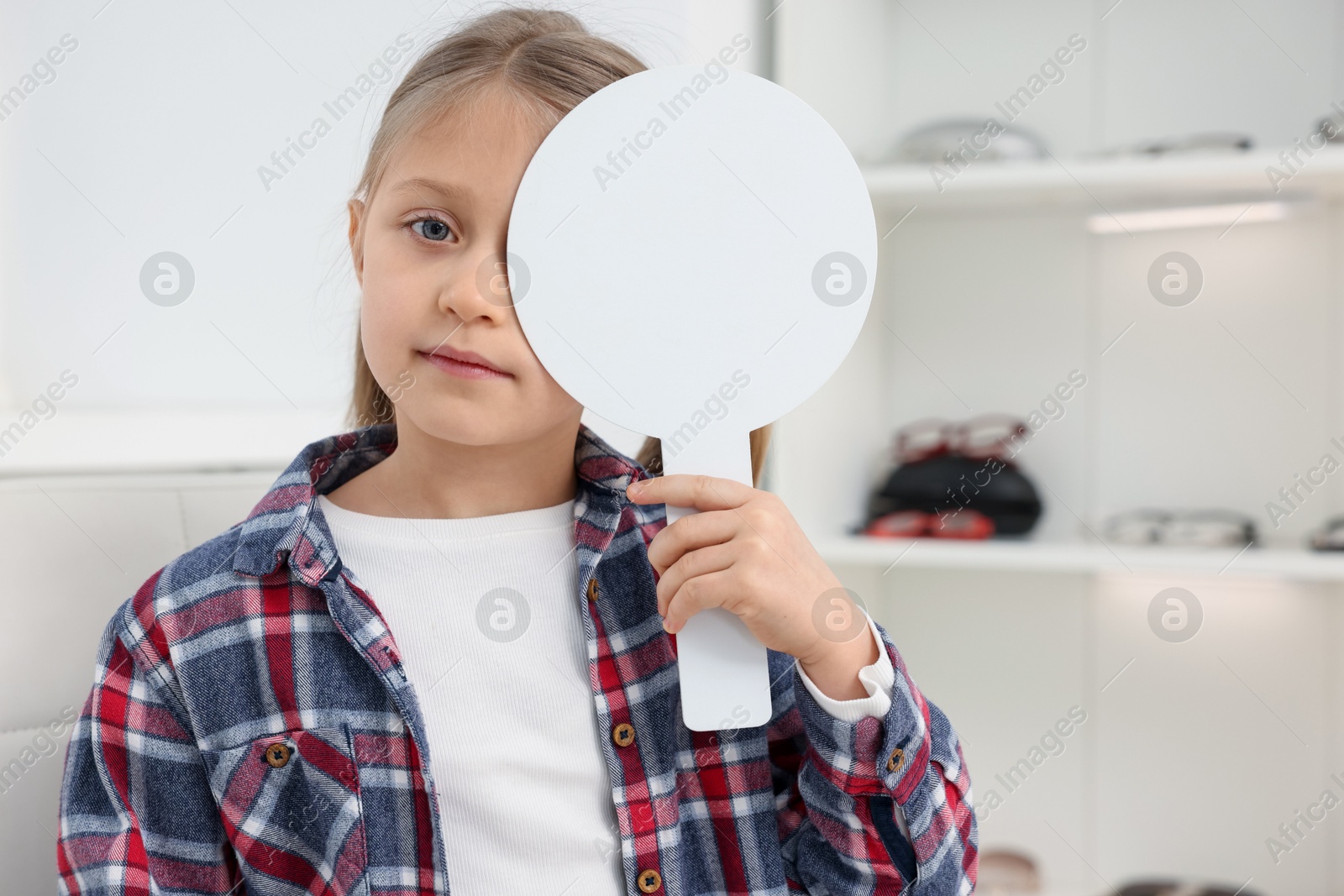 Photo of Little girl covering her eye at ophthalmologist office, space for text