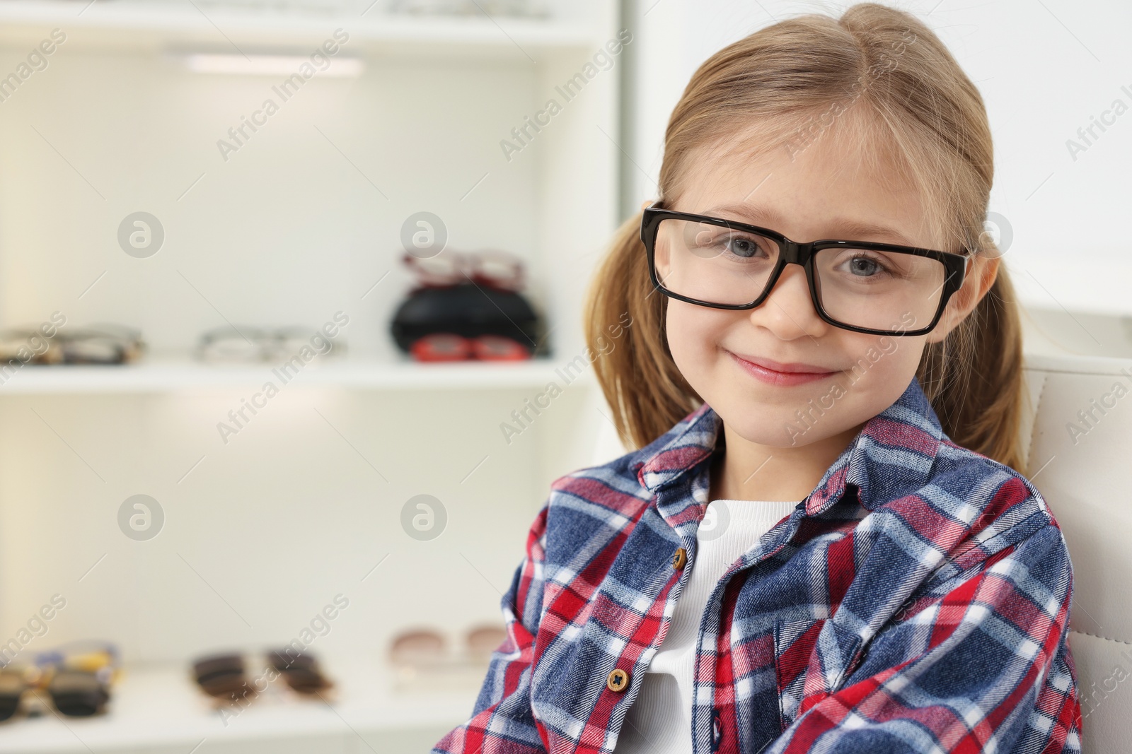 Photo of Little girl trying glasses at ophthalmologist office, space for text