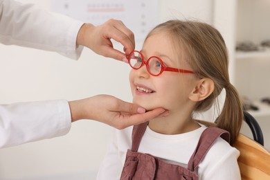 Photo of Vision testing. Ophthalmologist giving glasses to little girl in clinic, closeup