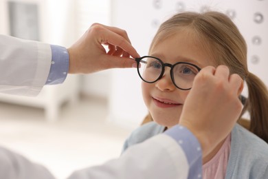 Photo of Vision testing. Ophthalmologist giving glasses to little girl indoors, closeup