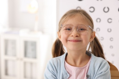 Photo of Little girl trying glasses at ophthalmologist office, space for text