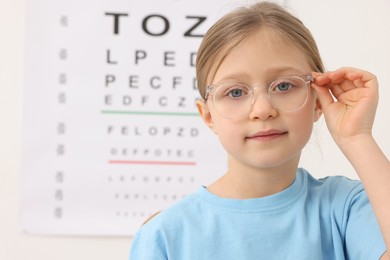 Photo of Little girl trying glasses against vision test chart