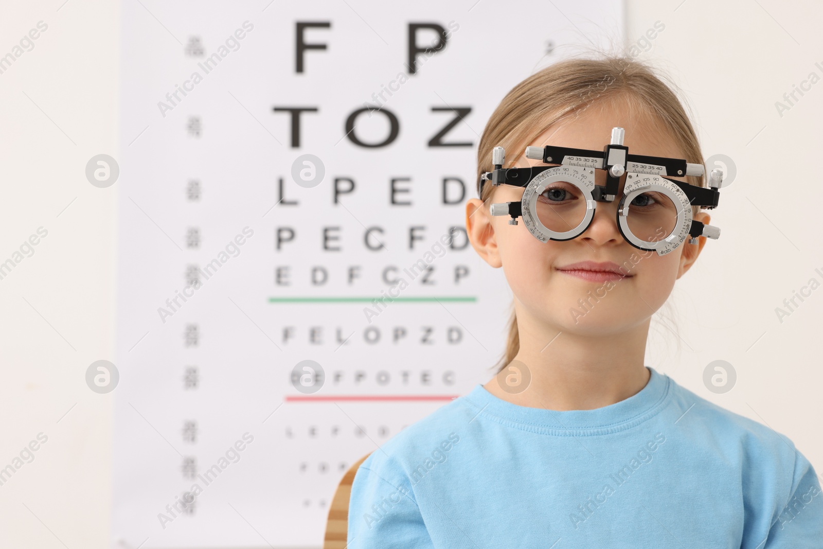 Photo of Little girl with trial frame against vision test chart. Eye examination