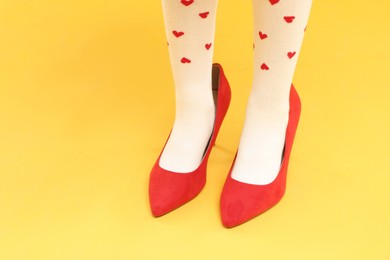 Photo of Little girl wearing oversized high heeled shoes on yellow background, closeup