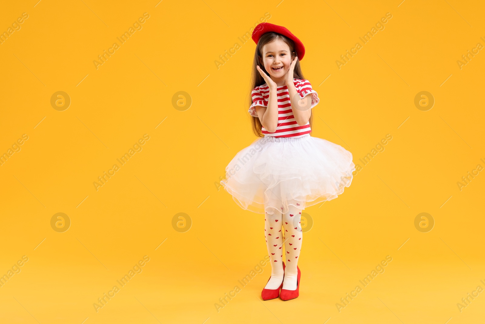 Photo of Stylish little girl wearing oversized high heeled shoes on orange background, space for text