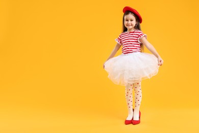 Photo of Stylish little girl wearing oversized high heeled shoes on orange background, space for text