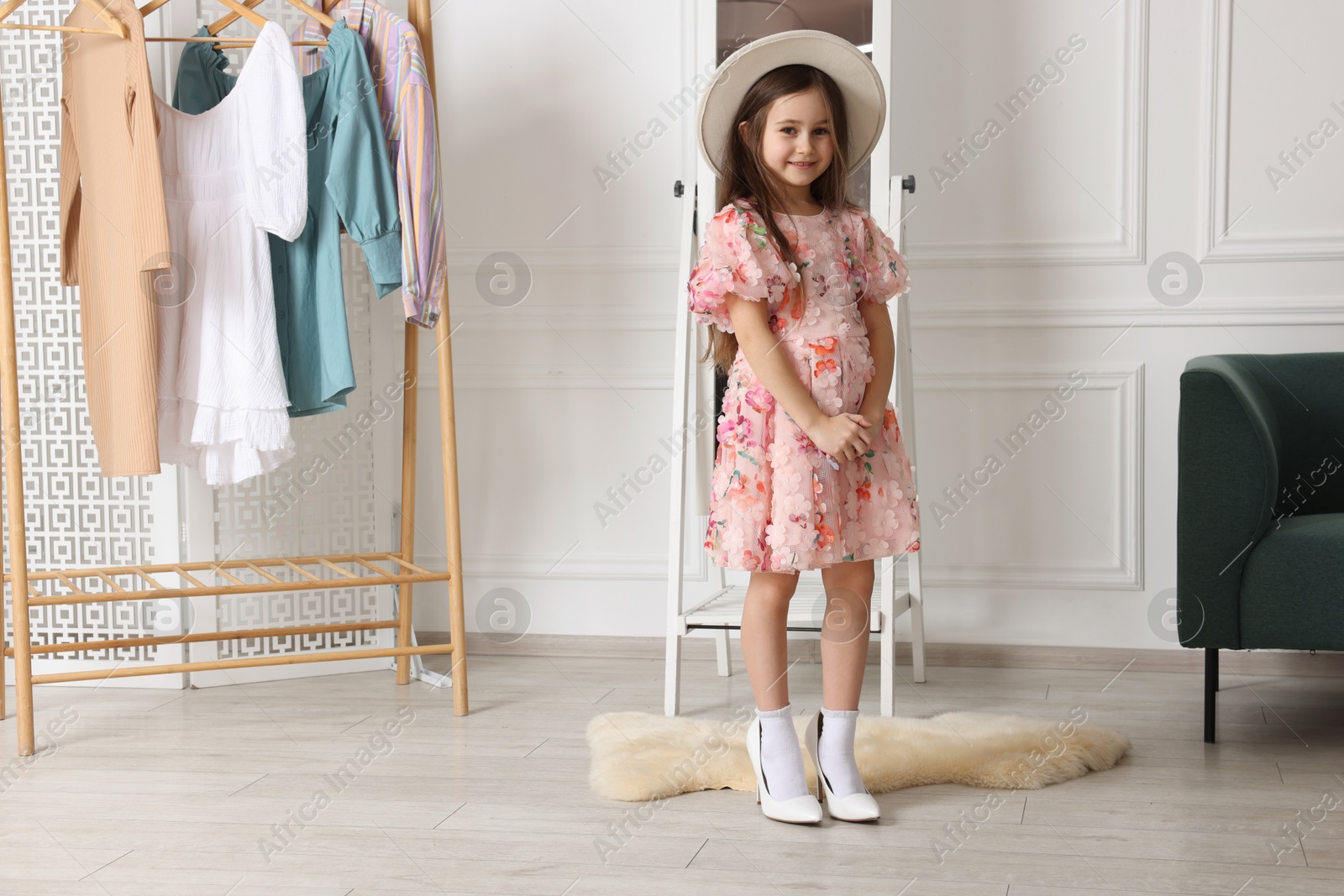 Photo of Stylish little girl wearing oversized high heeled shoes indoors