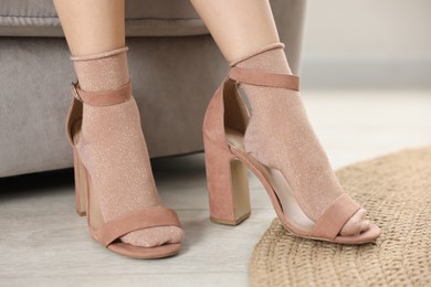 Photo of Little girl wearing oversized high heeled shoes indoors, closeup