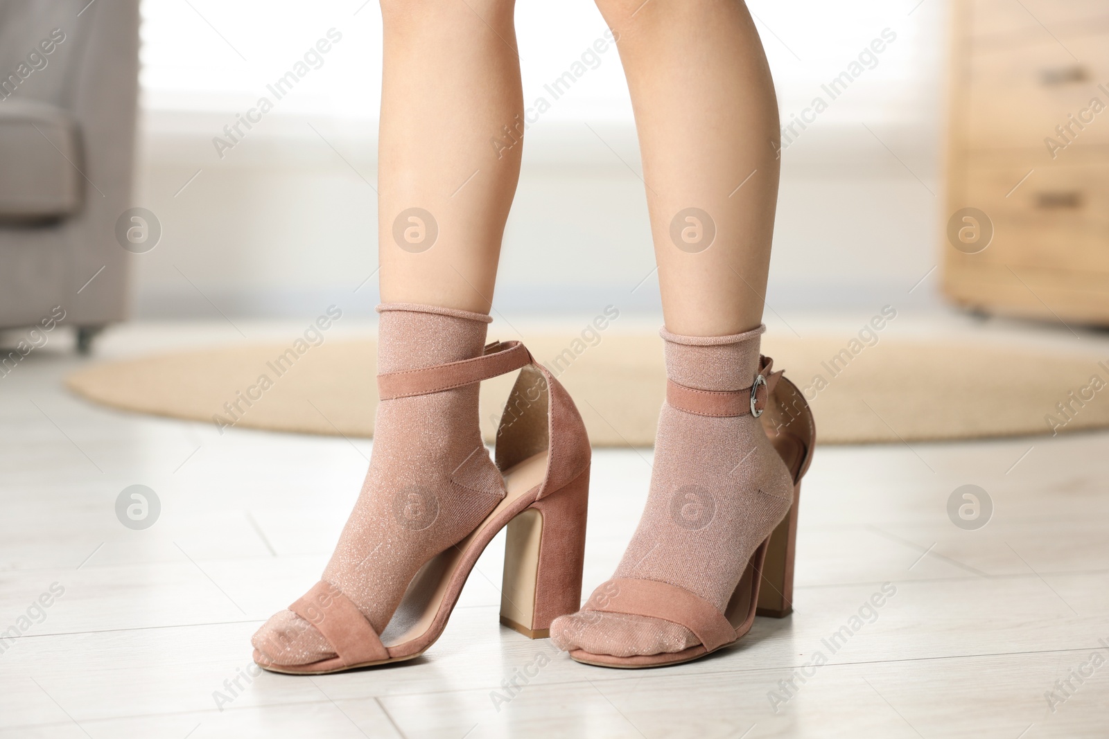 Photo of Little girl wearing oversized high heeled shoes indoors, closeup