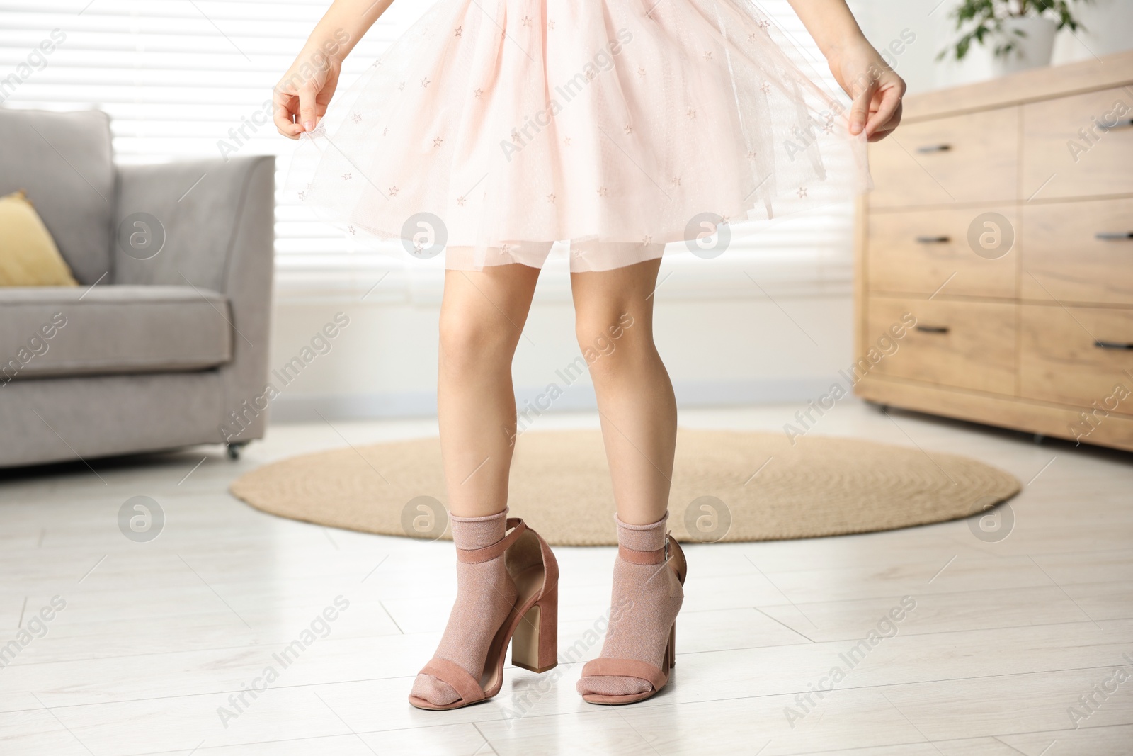 Photo of Little girl wearing oversized high heeled shoes indoors, closeup