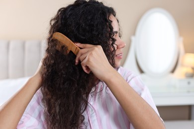 Photo of Young woman brushing her curly hair with comb at home