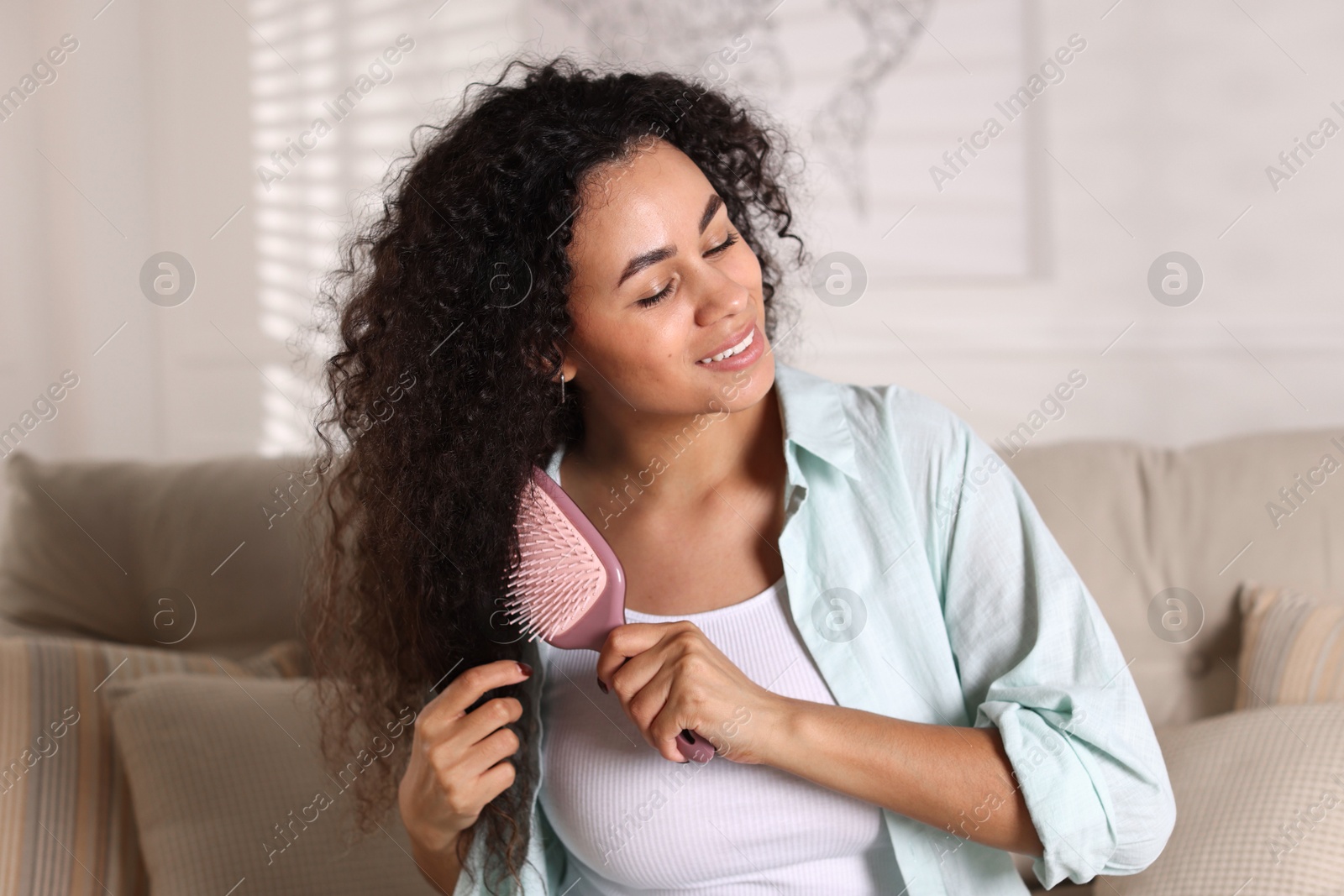 Photo of Smiling young woman brushing her curly hair at home