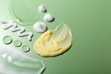 Photo of Cream and gel samples on green background, closeup. Space for text