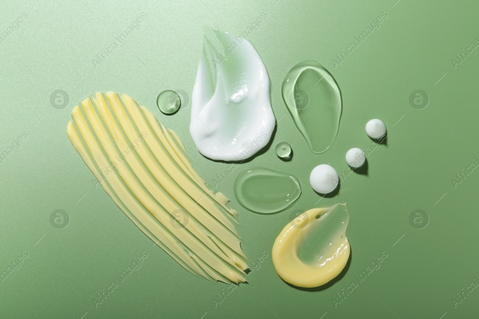 Photo of Cream and gel samples on green background, top view