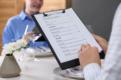 Photo of Couple choosing dishes from menu at table in restaurant, closeup