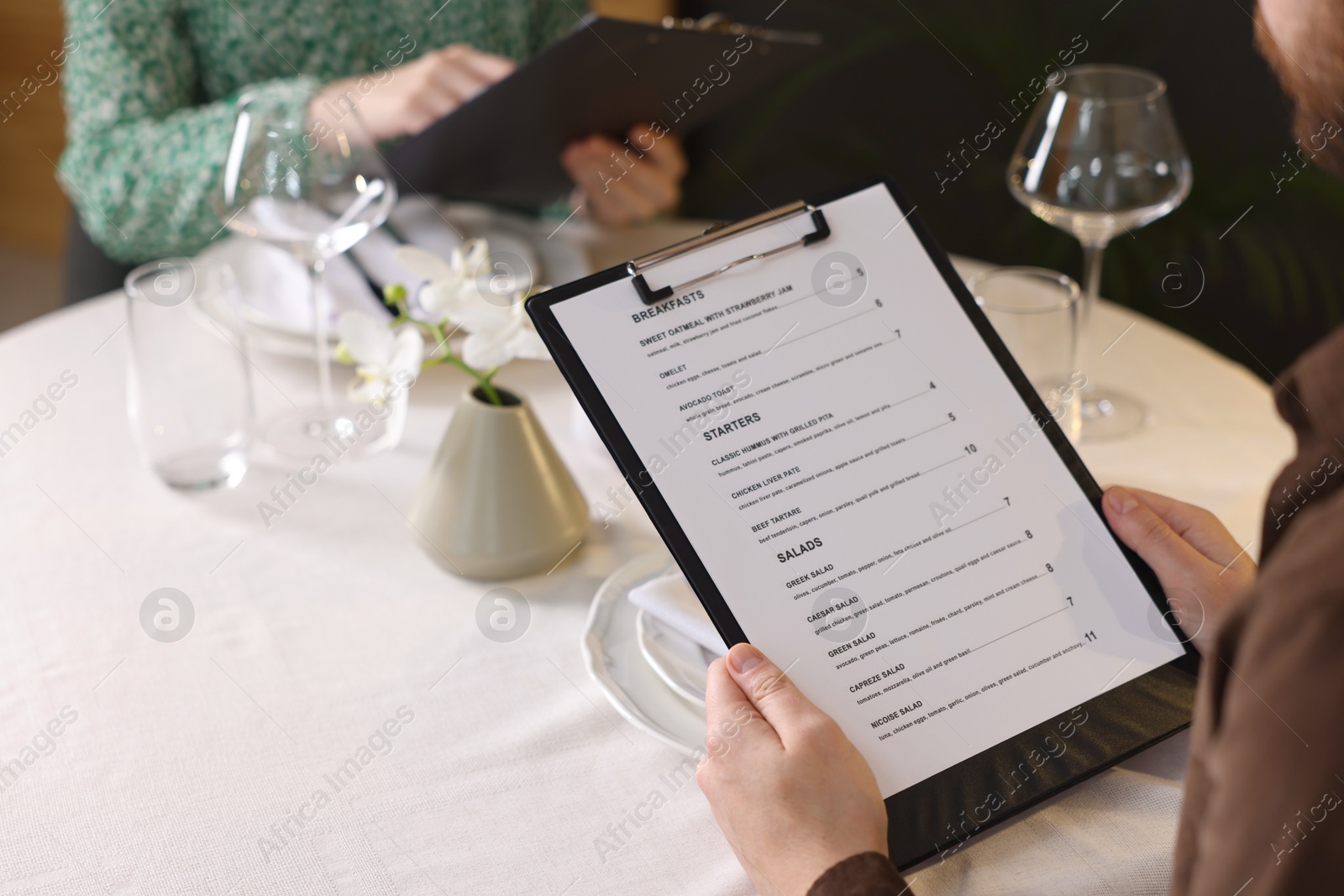 Photo of Couple choosing dishes from menu at table in restaurant, closeup