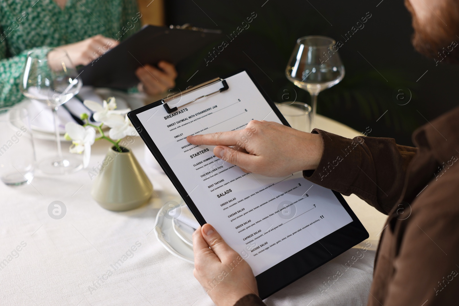 Photo of Couple choosing dishes from menu at table in restaurant, closeup