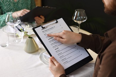 Photo of Couple choosing dishes from menu at table in restaurant, closeup