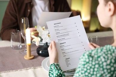 Photo of Couple choosing dishes from menu at table in restaurant, closeup