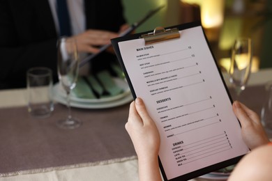 Photo of Couple choosing dishes from menu at table in restaurant, closeup