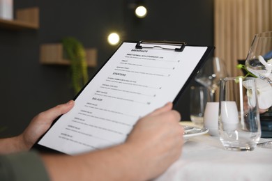 Photo of Man choosing dish from menu at table in restaurant, closeup