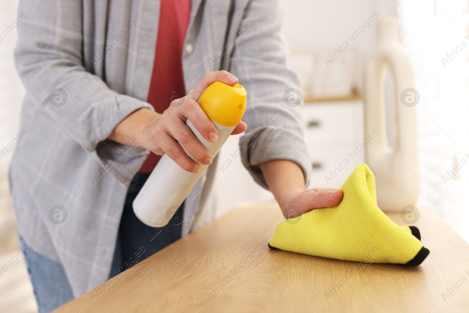 Photo of Woman using cleaning product while polishing wooden table with rag indoors, closeup