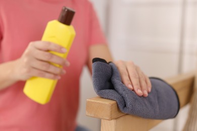 Photo of Woman with cleaning product and rag polishing wooden armrest at home, closeup