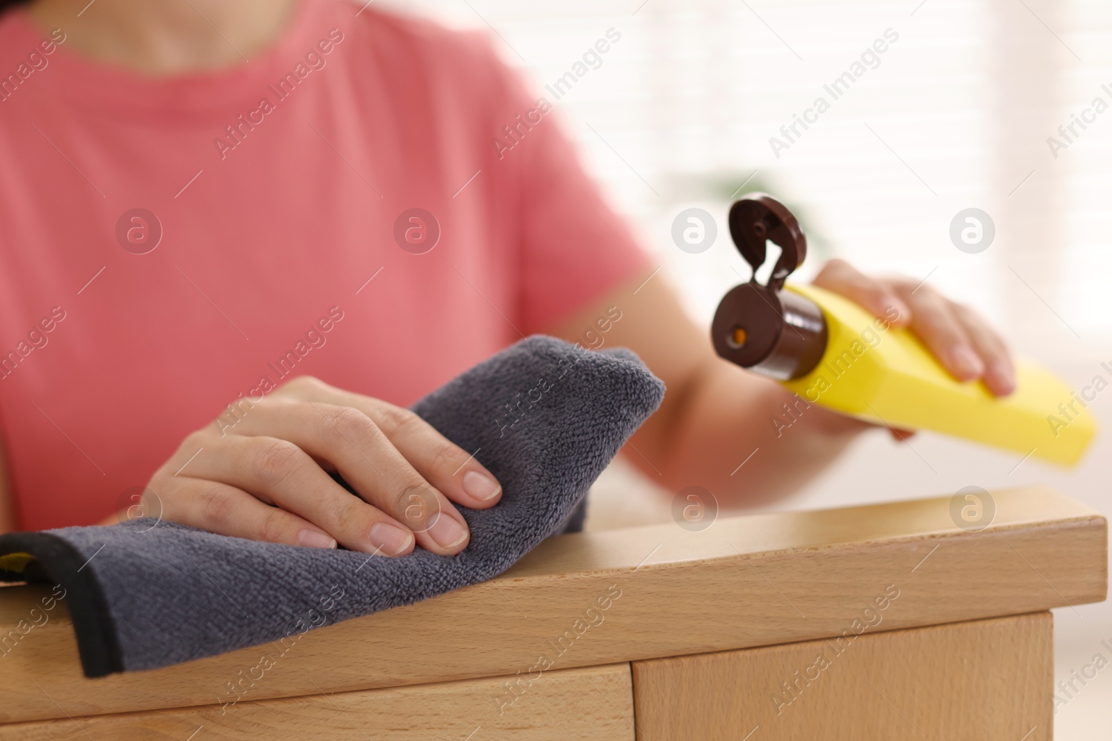 Photo of Woman with cleaning product and rag polishing wooden armrest at home, closeup