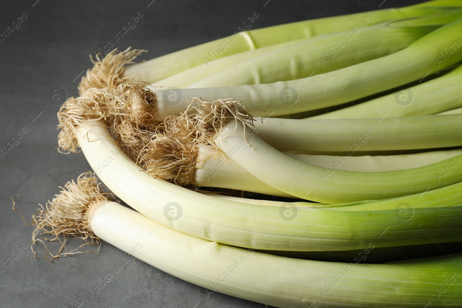 Photo of Fresh green leeks on grey table, closeup