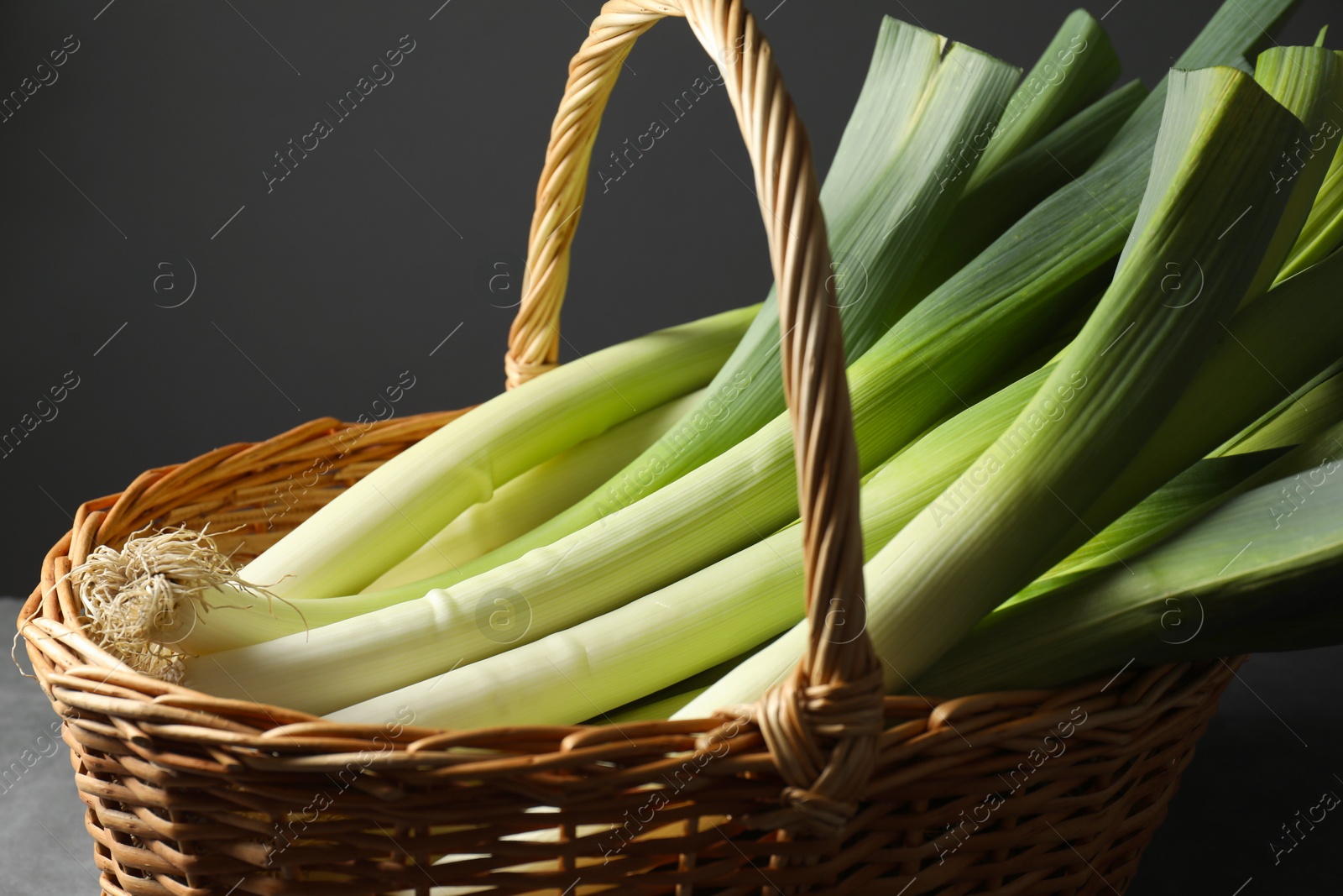 Photo of Fresh leeks in wicker basket on grey table, closeup