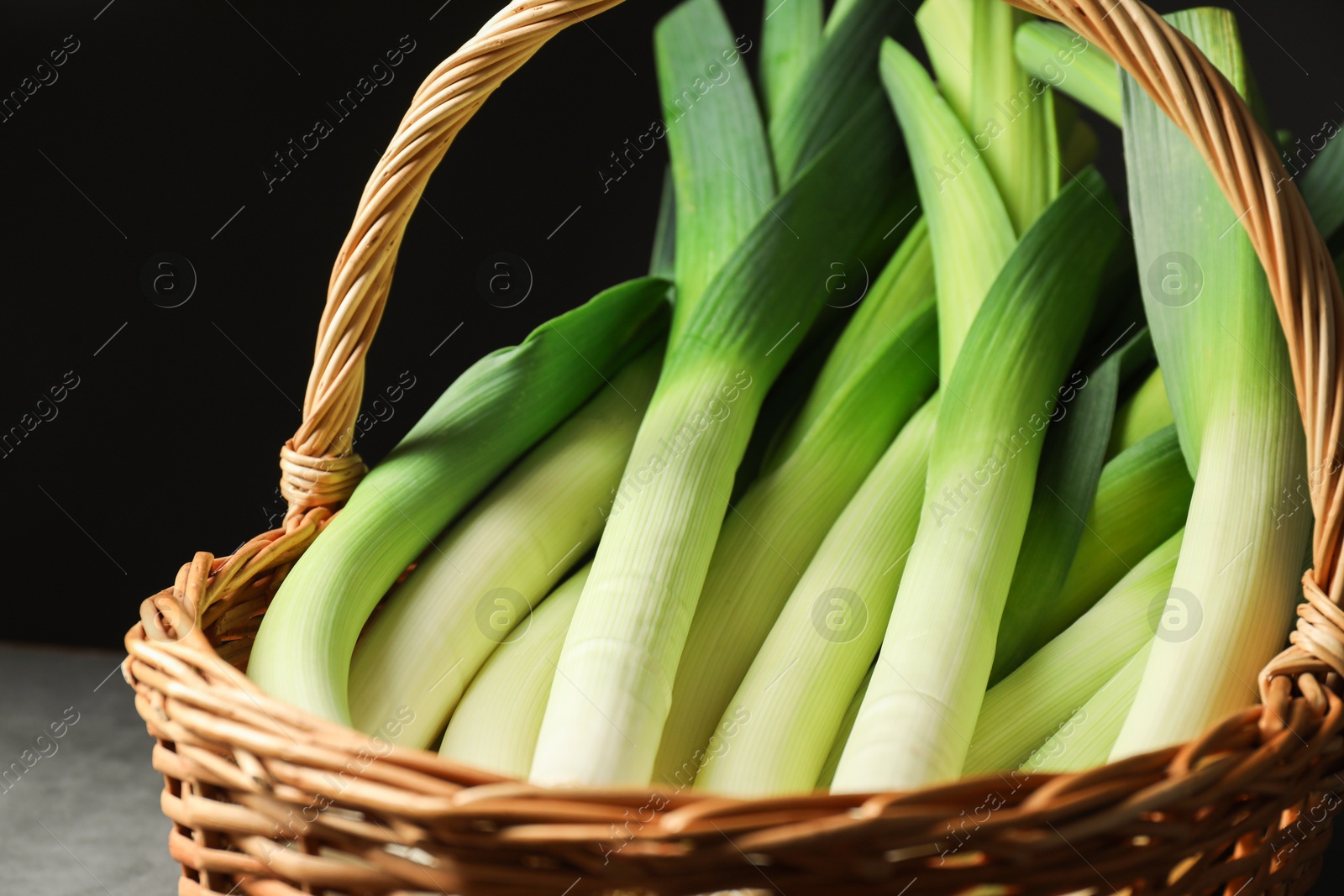 Photo of Fresh leeks in wicker basket on grey table, closeup