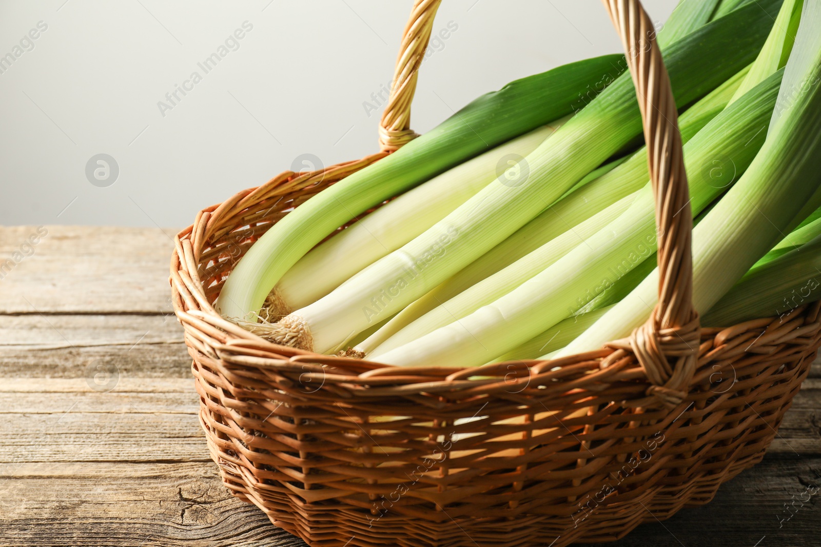 Photo of Fresh leeks in wicker basket on wooden table, closeup