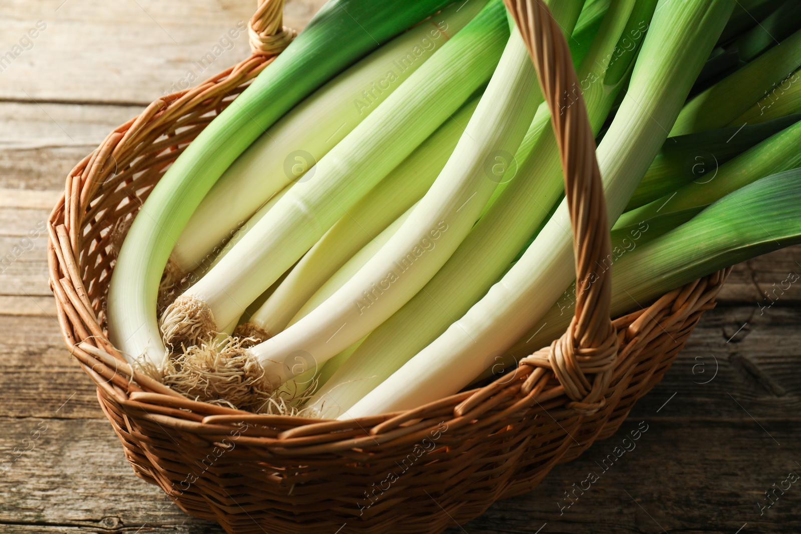 Photo of Fresh leeks in wicker basket on wooden table, closeup