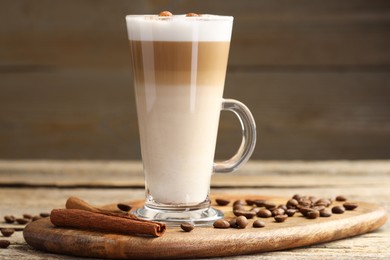 Photo of Tasty latte macchiato in glass cup, coffee beans and cinnamon on wooden table, closeup