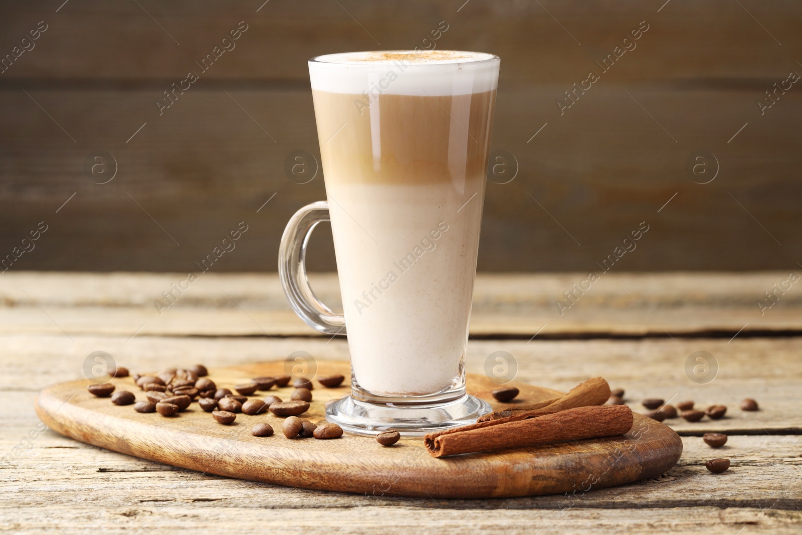 Photo of Tasty latte macchiato in glass cup, coffee beans and cinnamon on wooden table, closeup