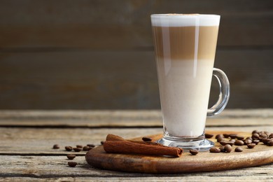 Photo of Tasty latte macchiato in glass cup, coffee beans and cinnamon on wooden table, closeup. Space for text