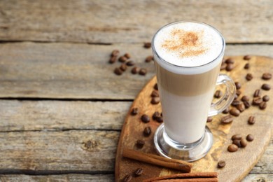 Photo of Tasty latte macchiato in glass cup, coffee beans and cinnamon on wooden table, closeup. Space for text