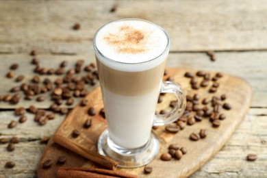 Photo of Tasty latte macchiato in glass cup, coffee beans and cinnamon on wooden table, closeup