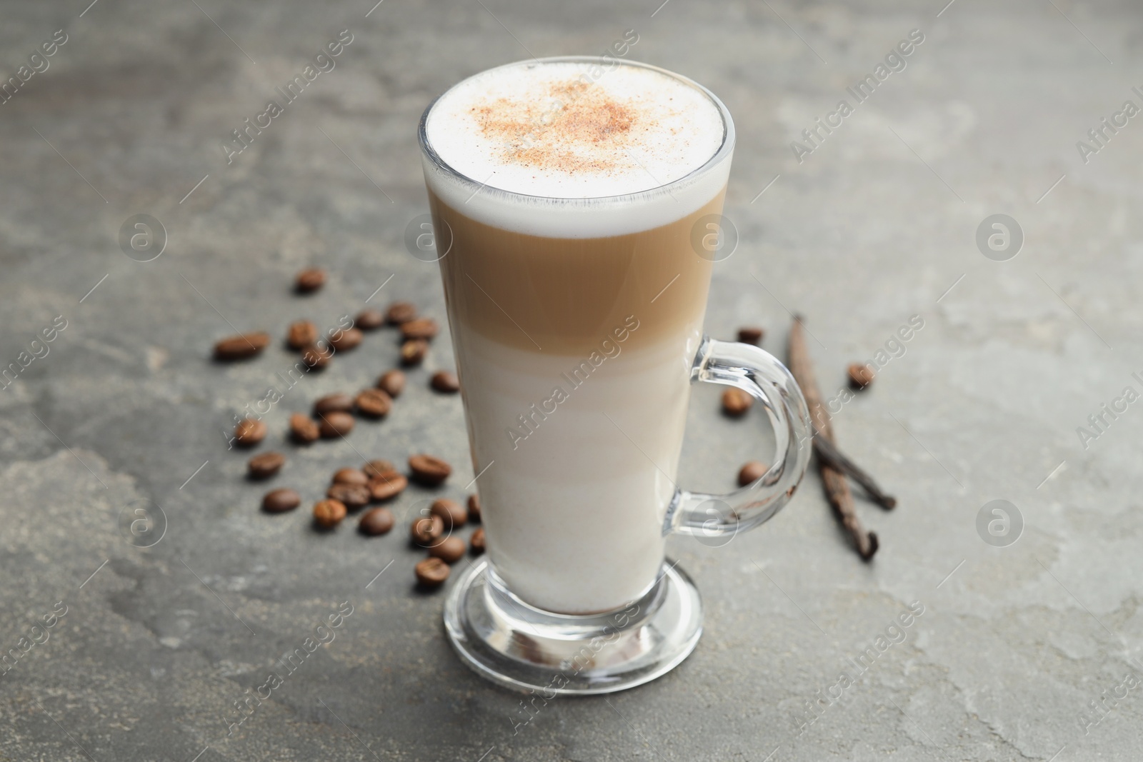 Photo of Tasty latte macchiato in glass cup, coffee beans and vanilla pods on grey table, closeup