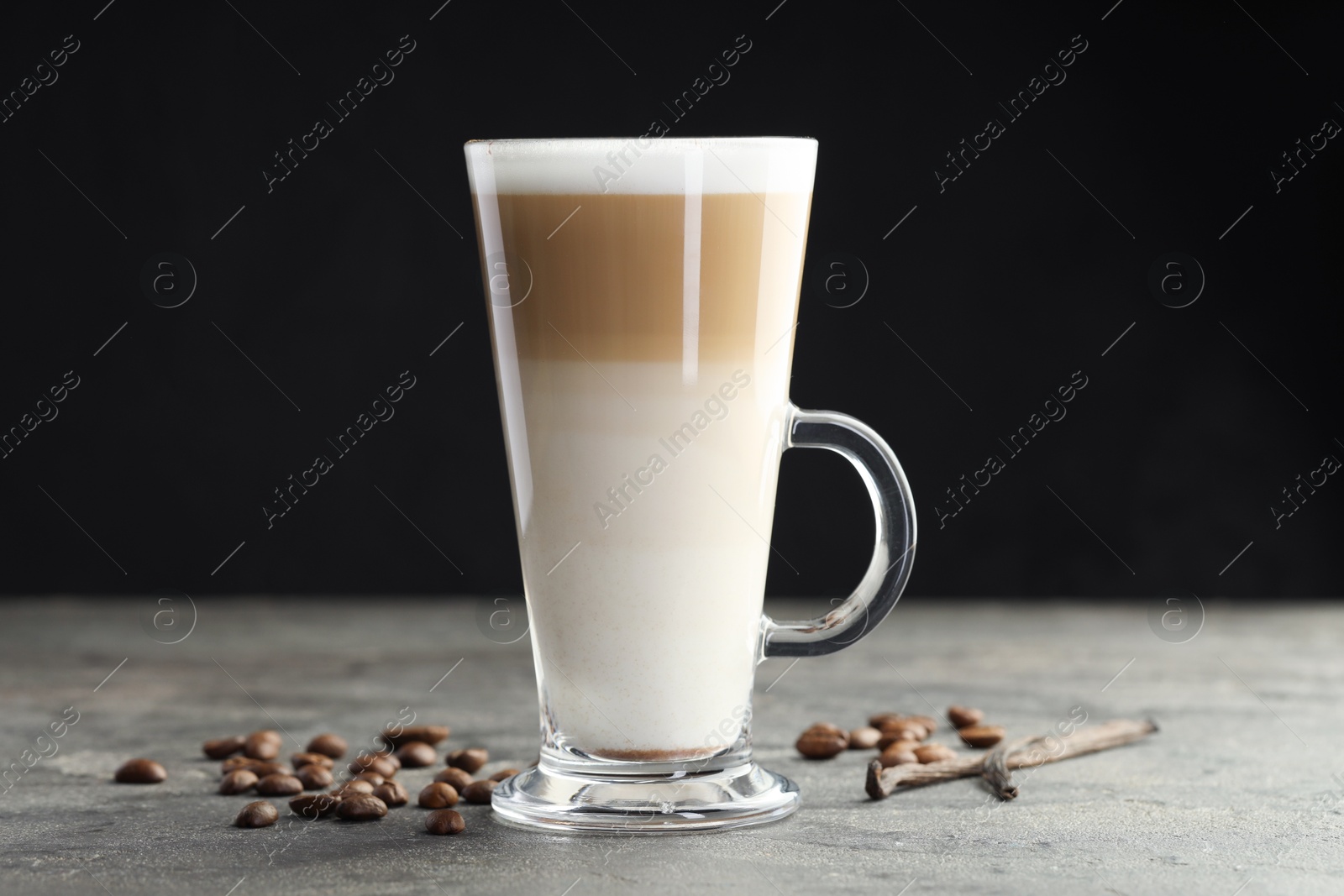 Photo of Tasty latte macchiato in glass cup, coffee beans and vanilla pods on grey table, closeup