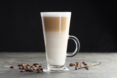 Photo of Tasty latte macchiato in glass cup, coffee beans and vanilla pods on grey table, closeup