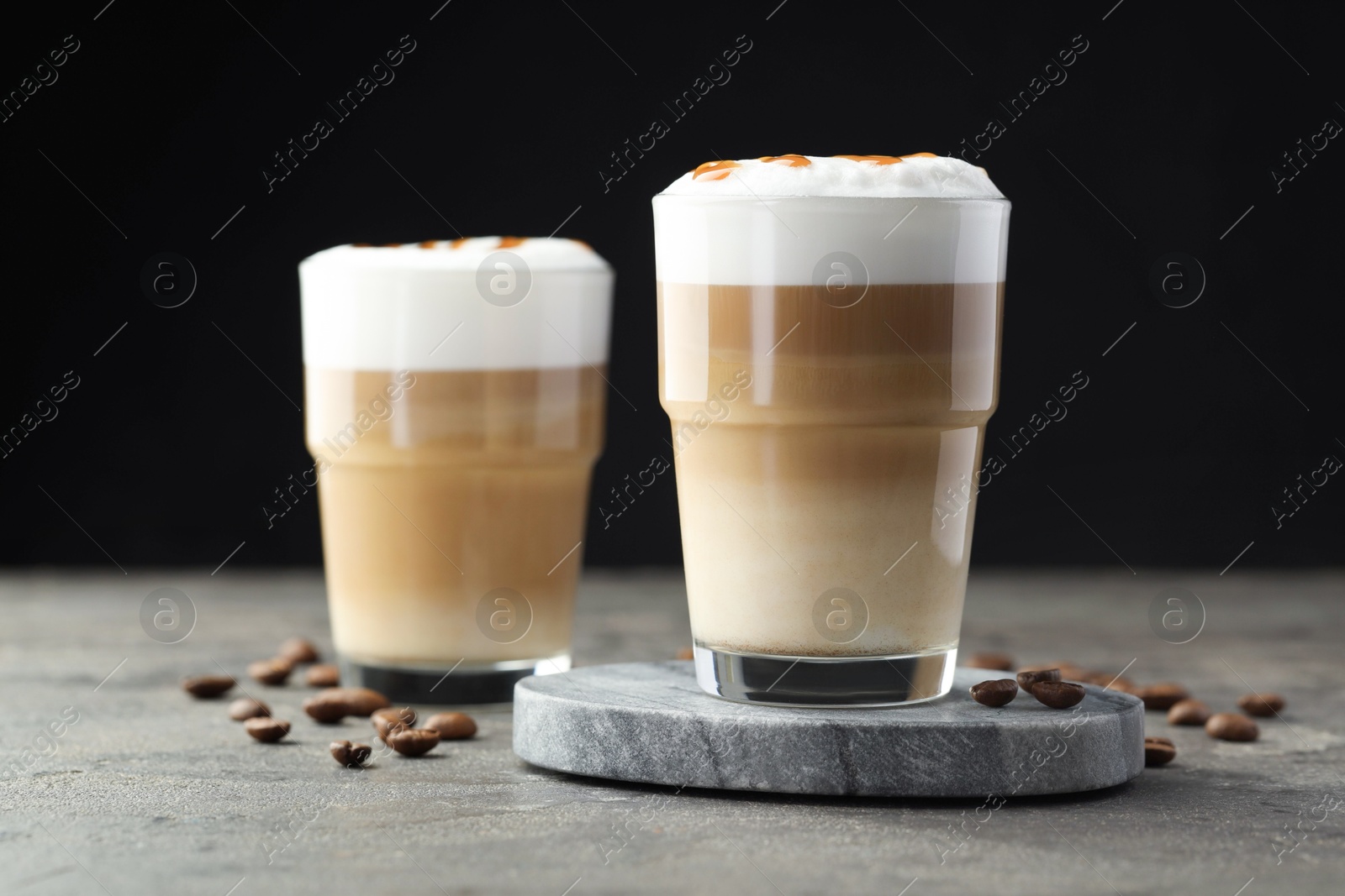 Photo of Tasty latte macchiato in glasses and coffee beans on grey table, closeup