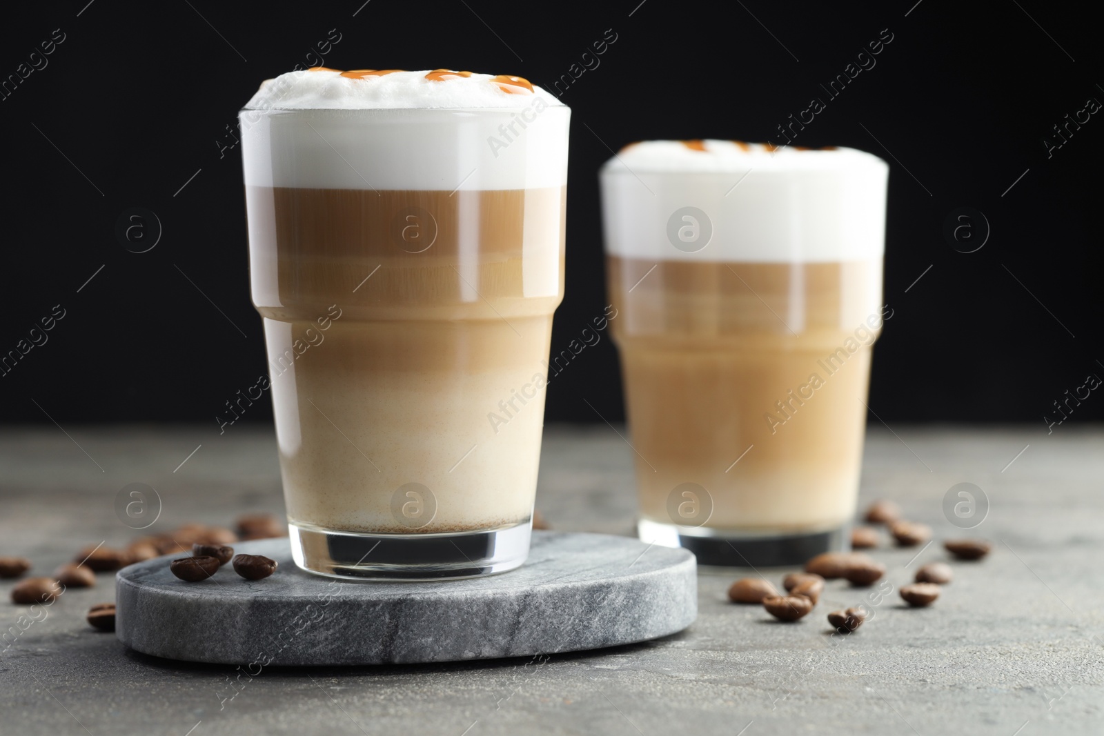 Photo of Tasty latte macchiato in glasses and coffee beans on grey table, closeup