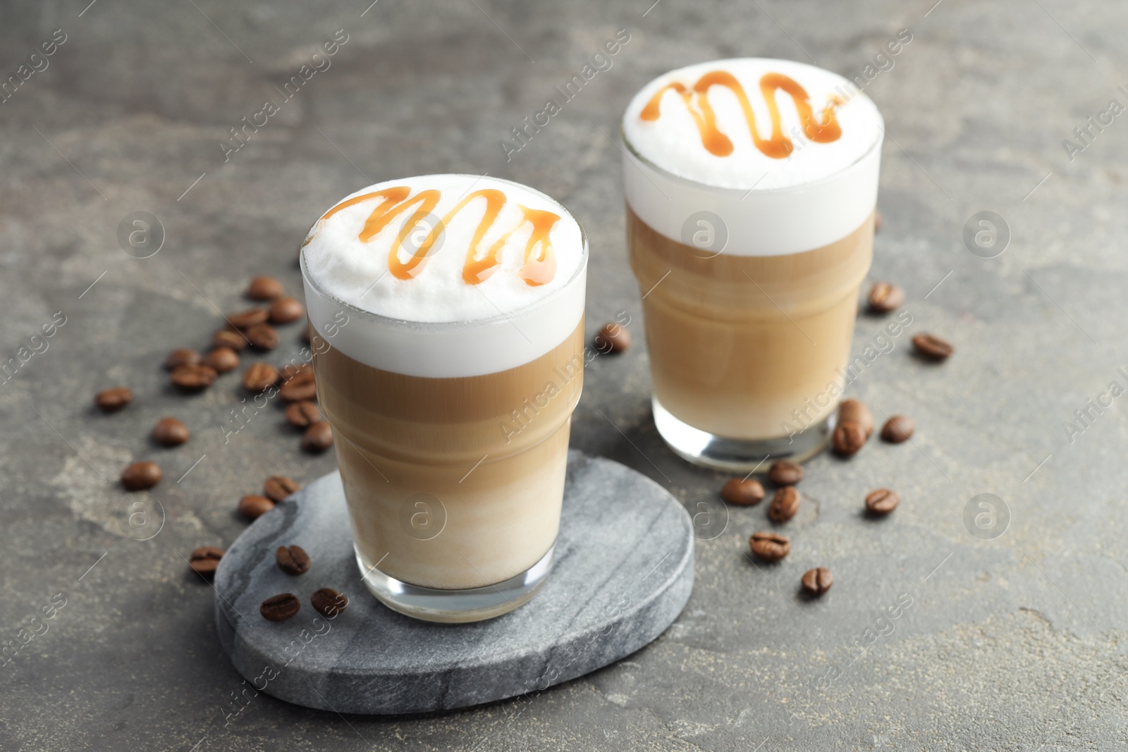 Photo of Tasty latte macchiato in glasses and coffee beans on grey table, closeup