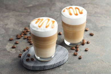 Photo of Tasty latte macchiato in glasses and coffee beans on grey table, closeup