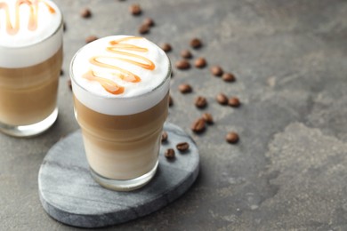 Photo of Tasty latte macchiato in glasses and coffee beans on grey table, closeup. Space for text